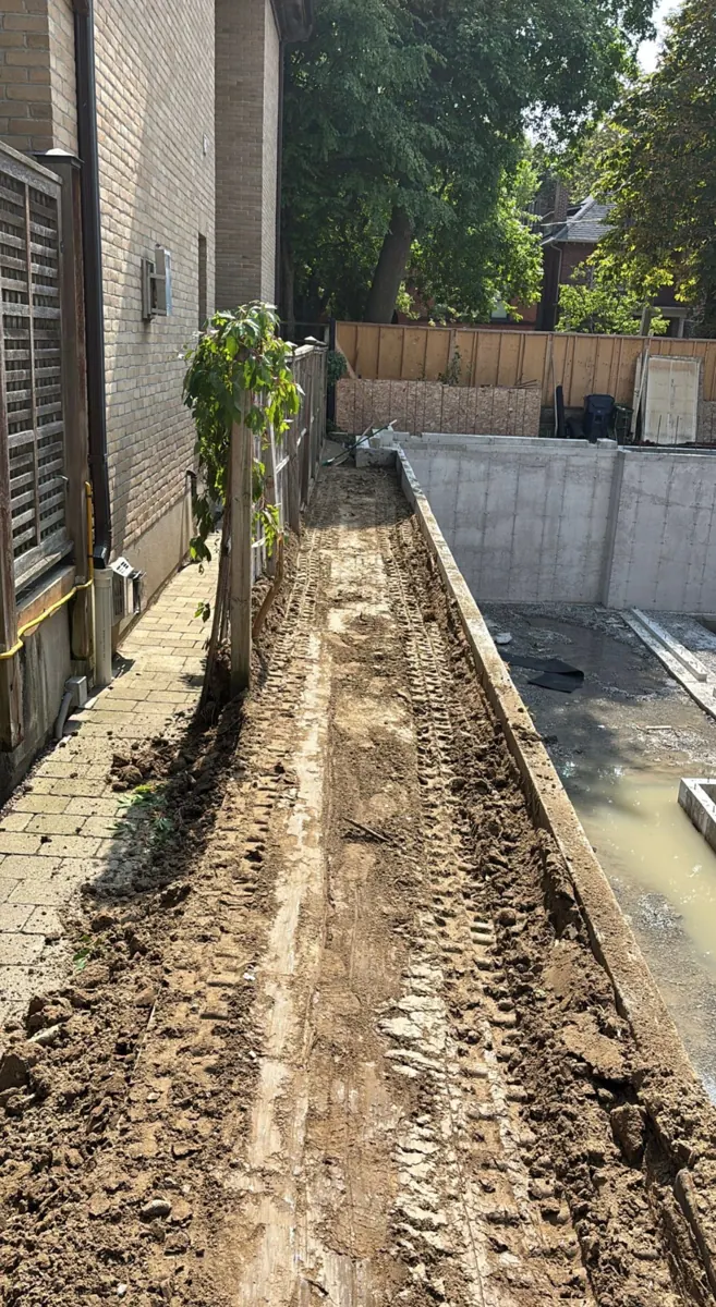 Compacted backfill placed in a narrow strip beside a new concrete foundation wall